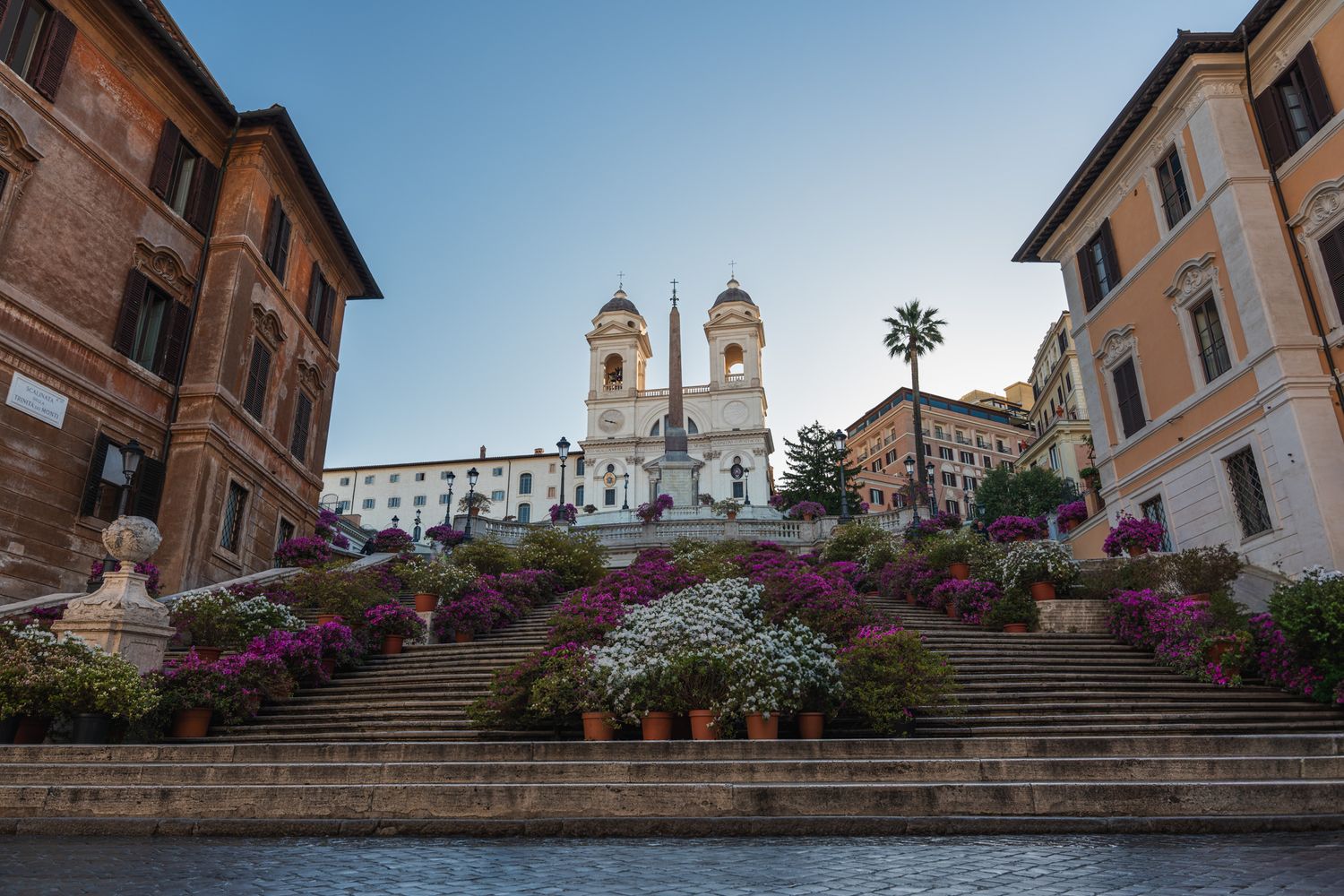 The Spanish Steps in Rome adorned with vibrant pink flowers and crowned by Trinita dei Monti church.