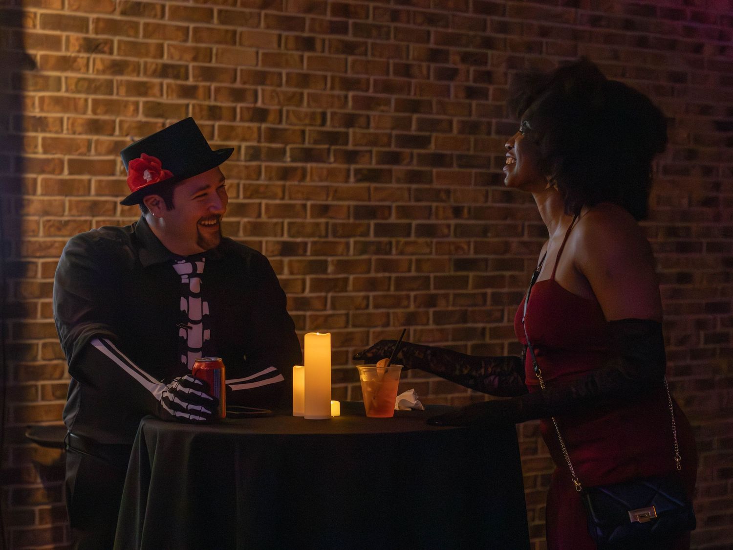 Couple enjoying drinks at candlelit table in brick-walled restaurant.