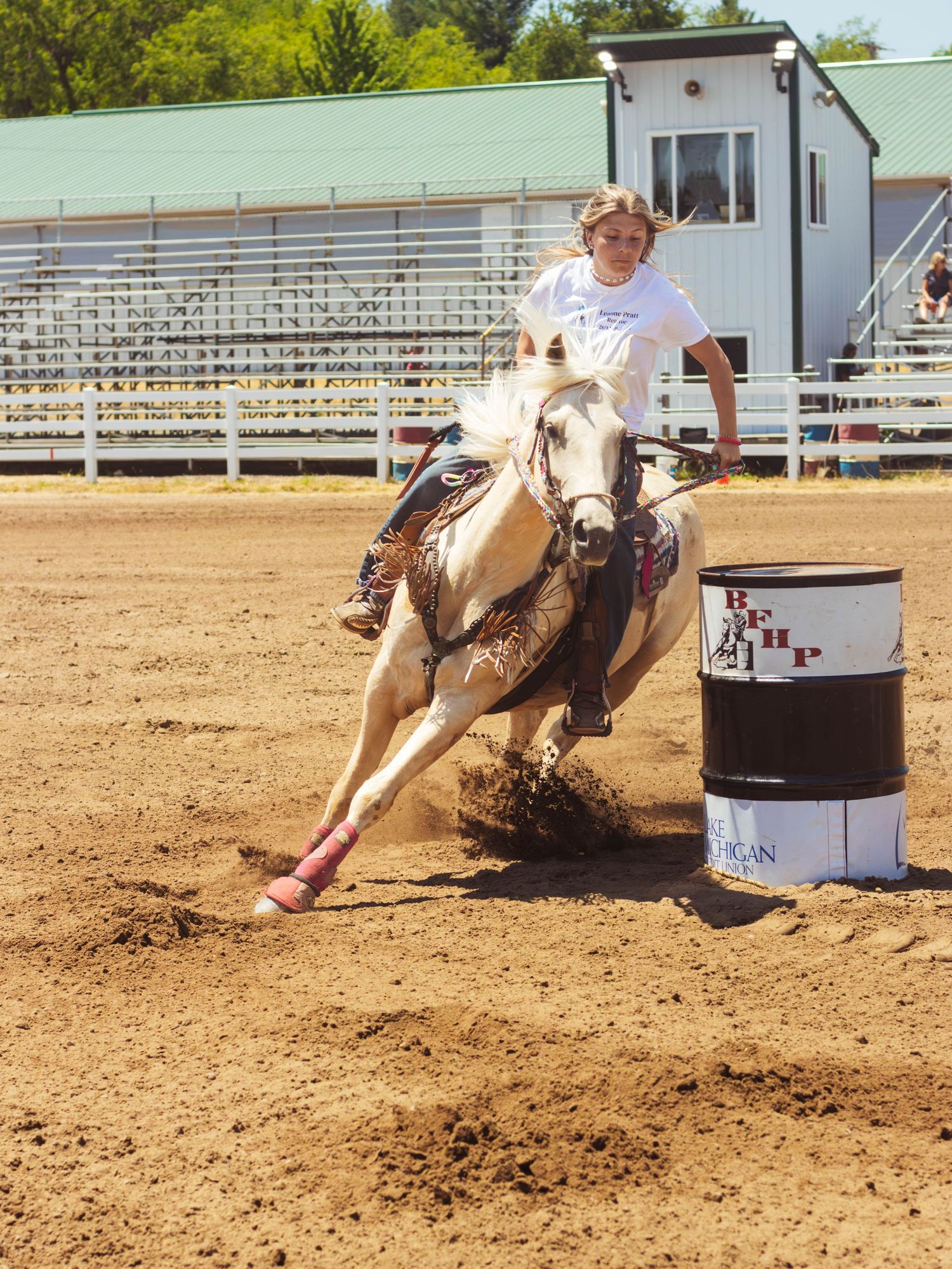 Barrel racer on light colored horse makes sharp turn during competition at outdoor arena.