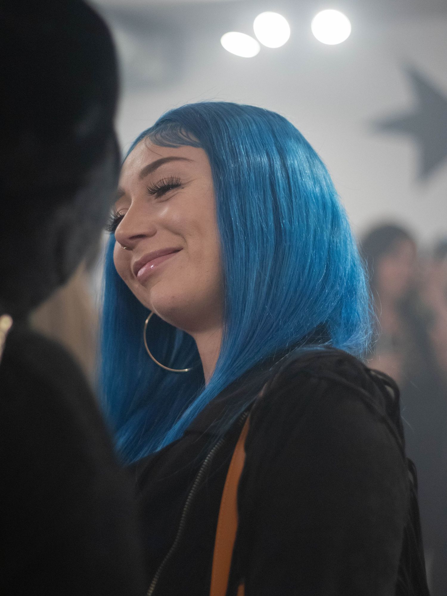 Someone with vibrant blue hair and hoop earrings smiling in a crowd.