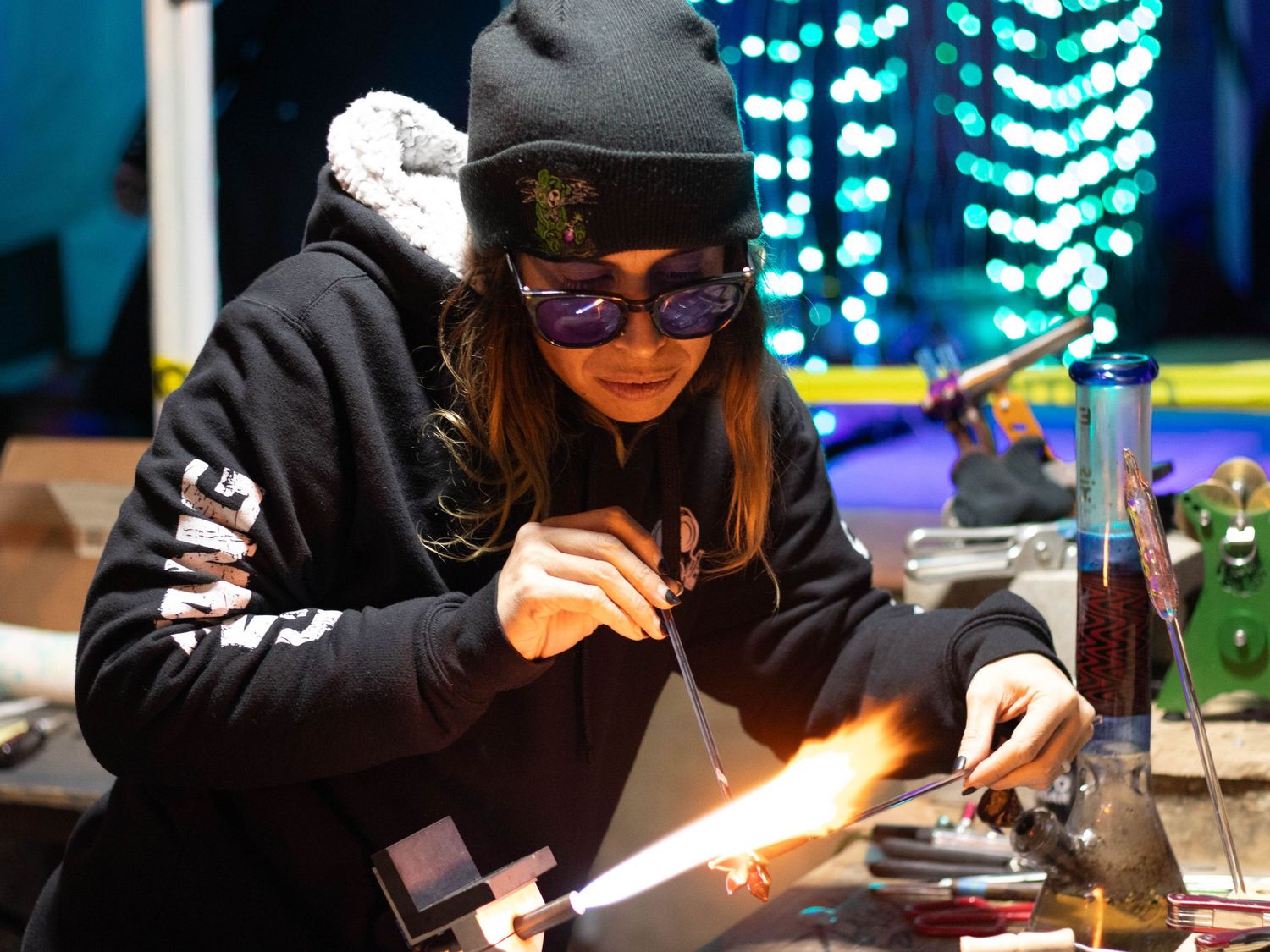 Person wearing winter gear lighting objects on table with colorful lights in background.