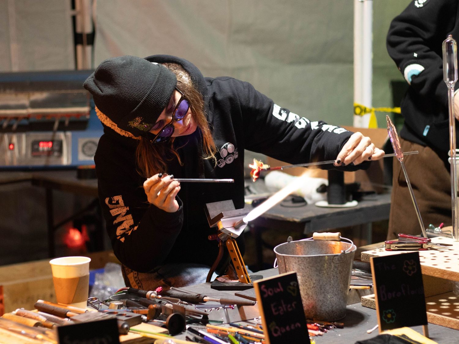 Person in black hoodie leaning over table with equipment and tools.