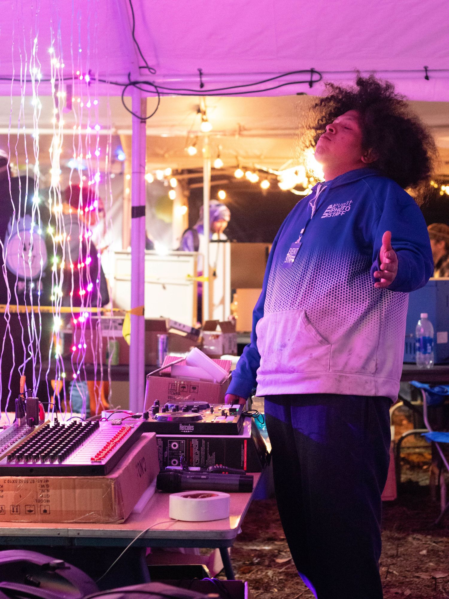 DJ in a blue gradient jacket performing under pink lighting at a venue.