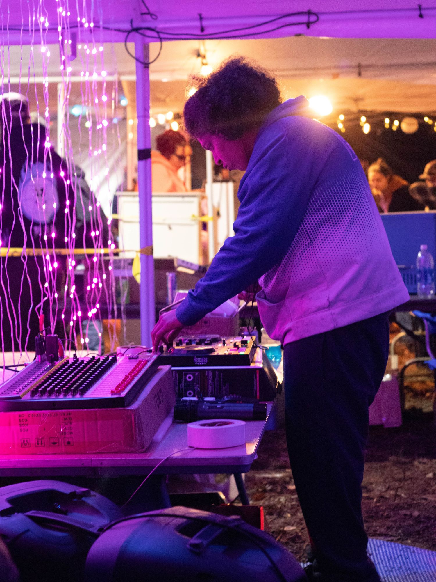 DJ performing with equipment under purple lighting at an indoor event.