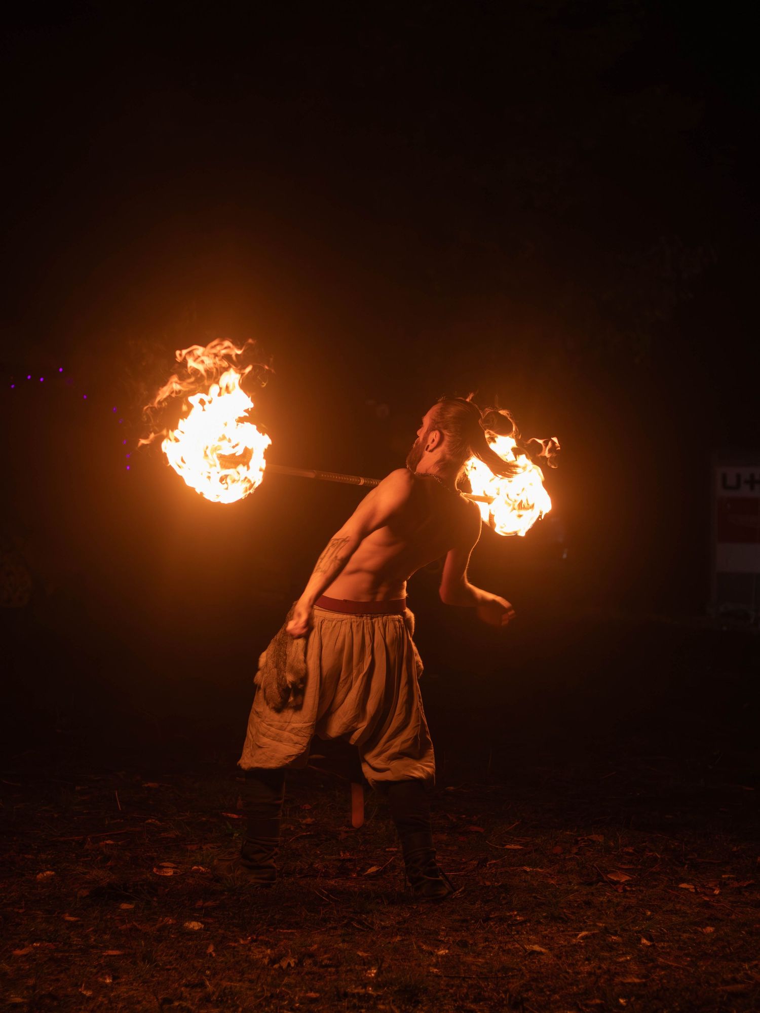 Fire performer spinning dual fire staffs at night creating dramatic light trails.