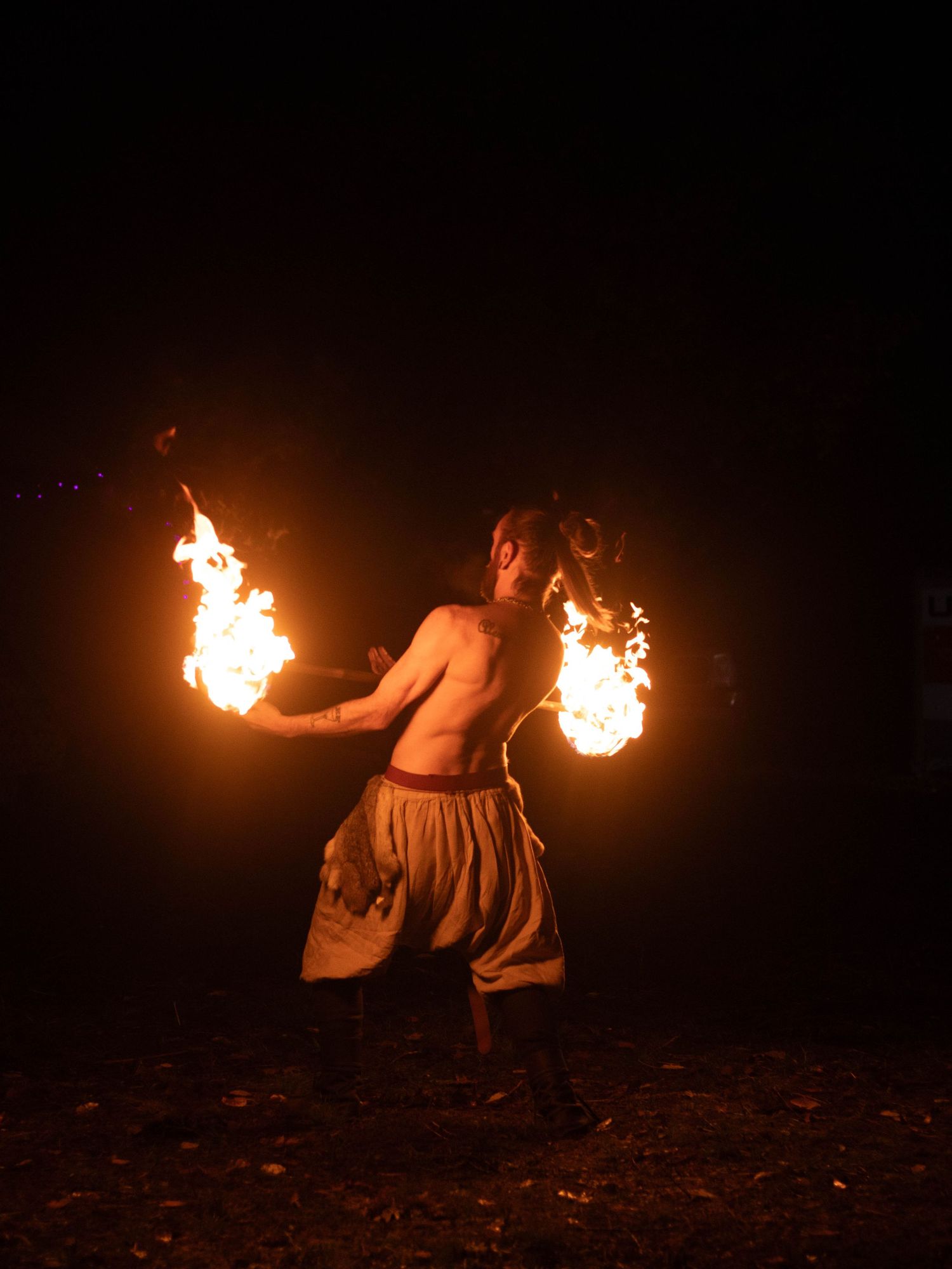 Fire performer spinning dual flaming torches against dark night sky background.