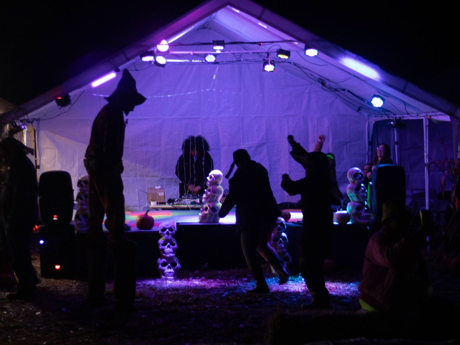 Silhouettes of people dancing under purple-lit tent at night event.