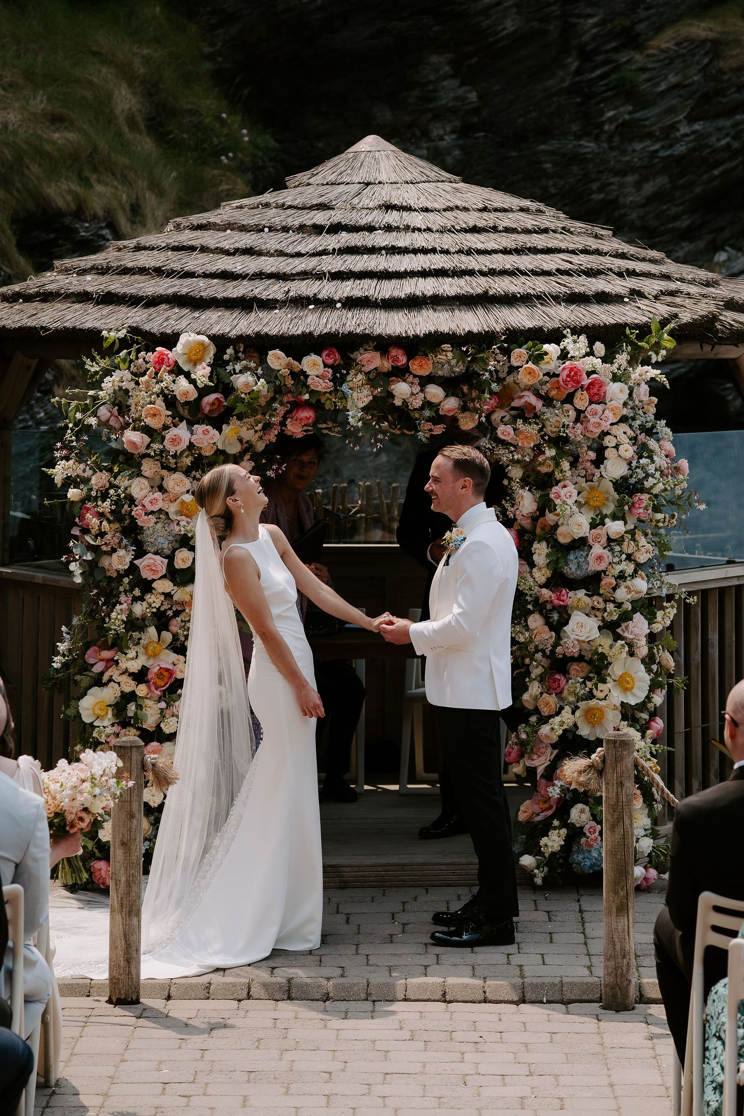 Bride and Groom in front of floral arch exchanging rings at Tunnels Beach Wedding Venue in North Devon