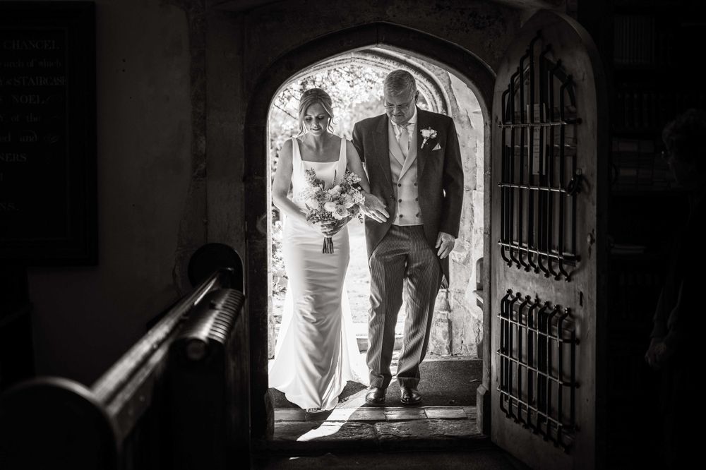Black and white wedding photo showing a couple entering through an arched doorway during their ceremony.