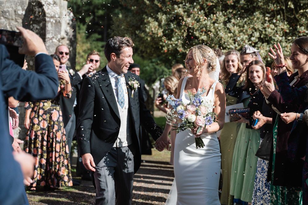 Newlywed couple walks down outdoor path surrounded by guests celebrating their wedding ceremony.