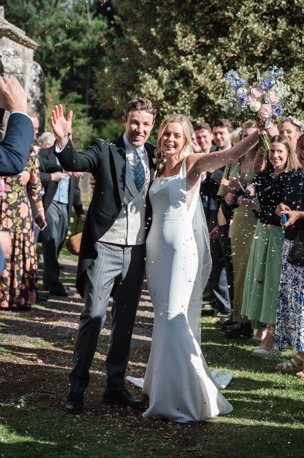 Joyful couple celebrates with guests on their wedding day as confetti showers down in a garden setting.