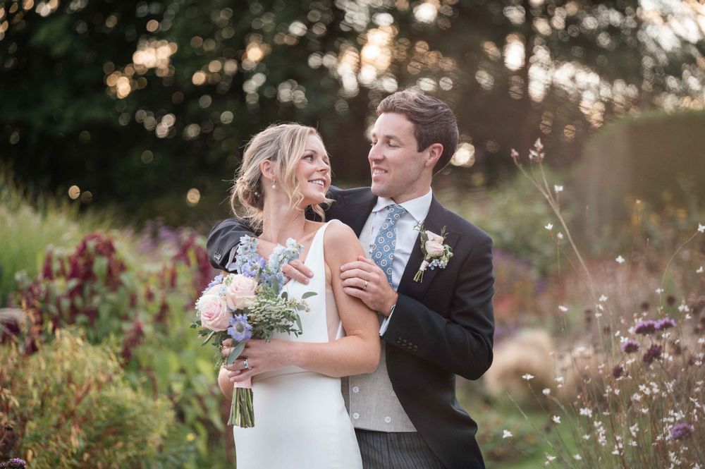 Wedding couple embraces tenderly in a garden of wildflowers during golden hour.
