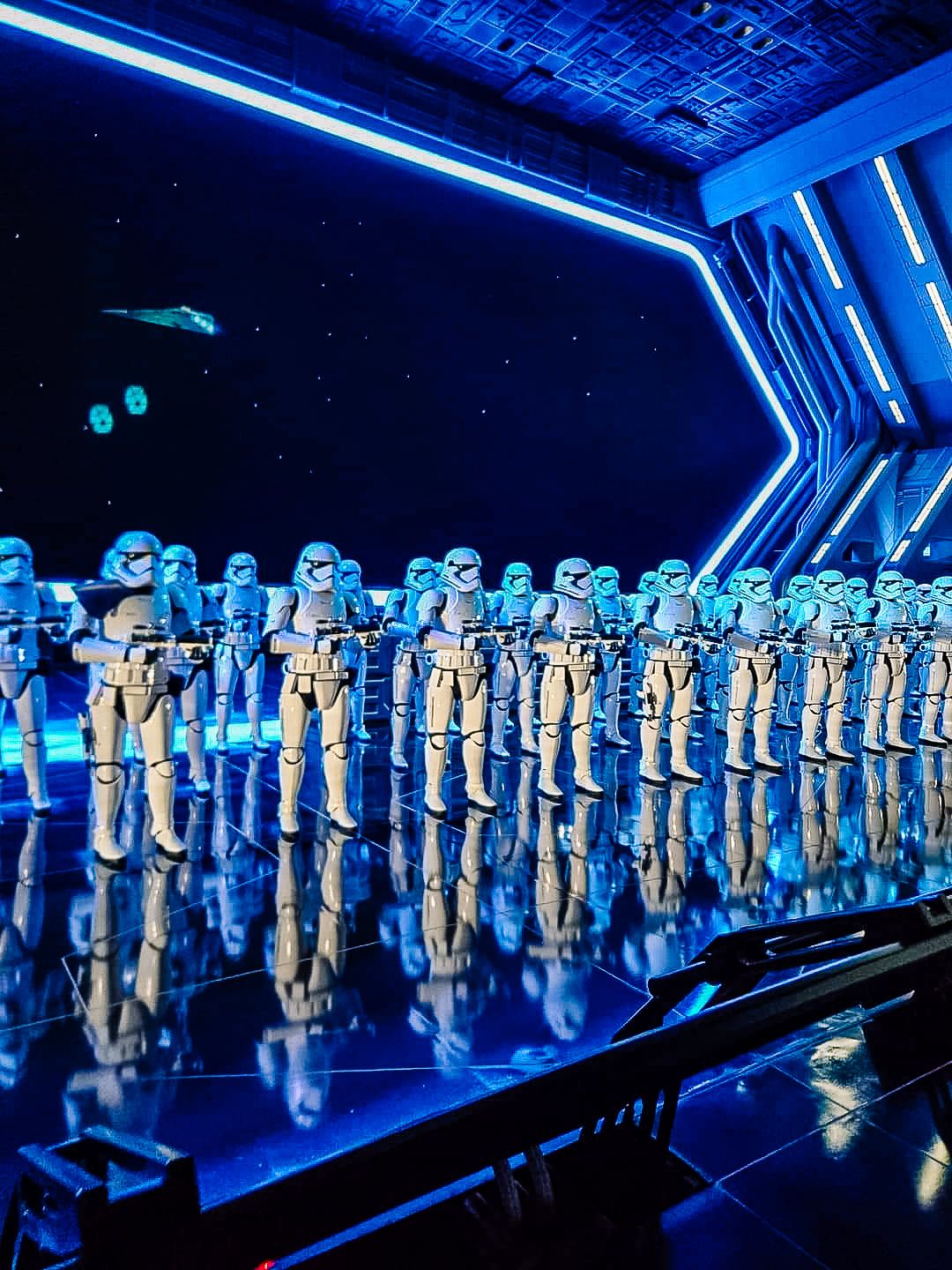 A row of Imperial Stormtrooper costumes from Star Wars illuminated with dramatic blue lighting in a dark exhibition space.