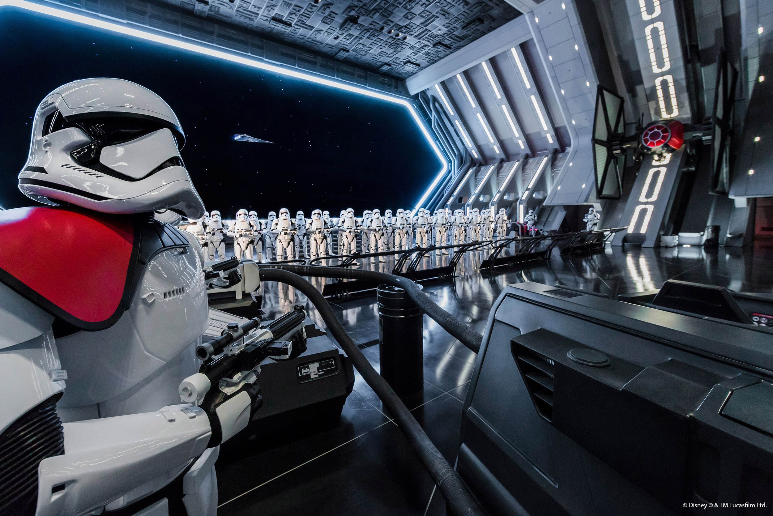 First Order Stormtroopers stand in formation inside a sleek, futuristic Star Wars-themed attraction at Disney.