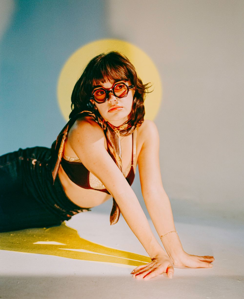 Stylized photo with yellow lighting of a model in sunglasses lounging on the ground.