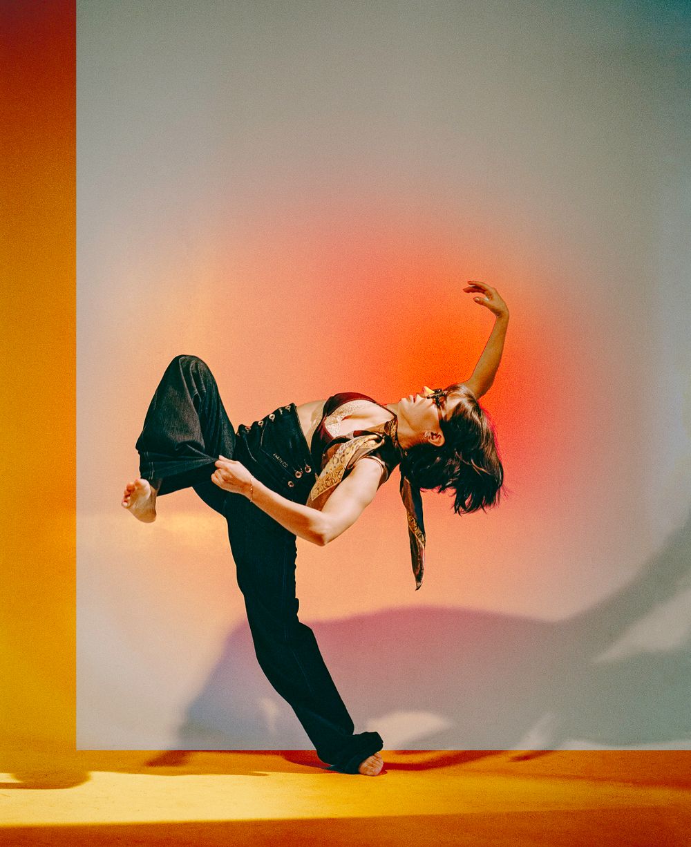 Dynamic dance pose silhouetted against a vibrant orange and pink gradient background.