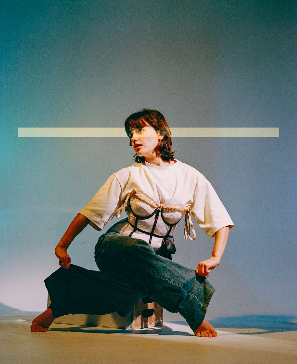 Contemporary fashion photo with model in white t-shirt and creative corset styling against blue backdrop.
