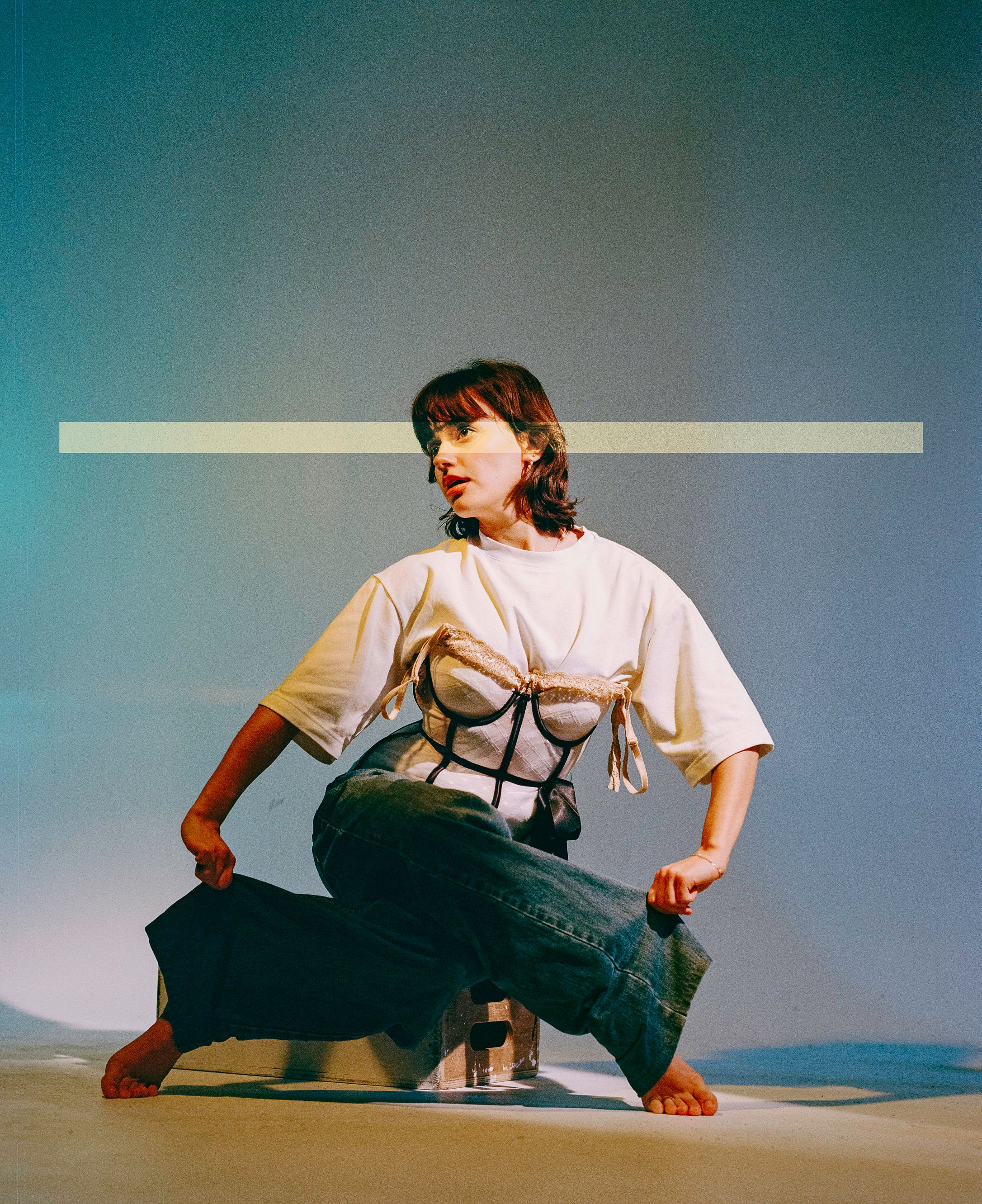 Contemporary fashion photo with model in white t-shirt and creative corset styling against blue backdrop.