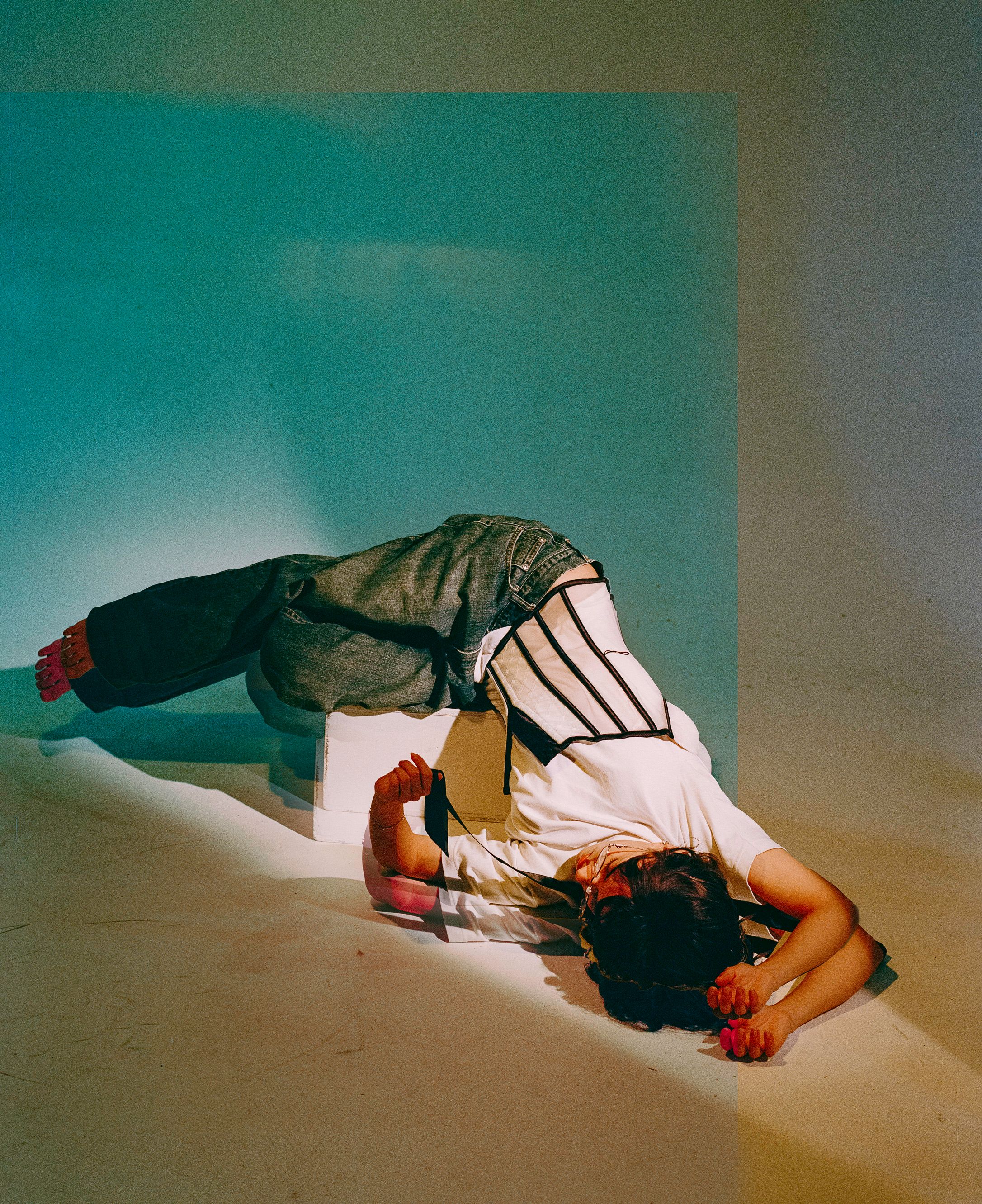 Artistic fashion photo showing model in layered clothing lying down with dramatic lighting.