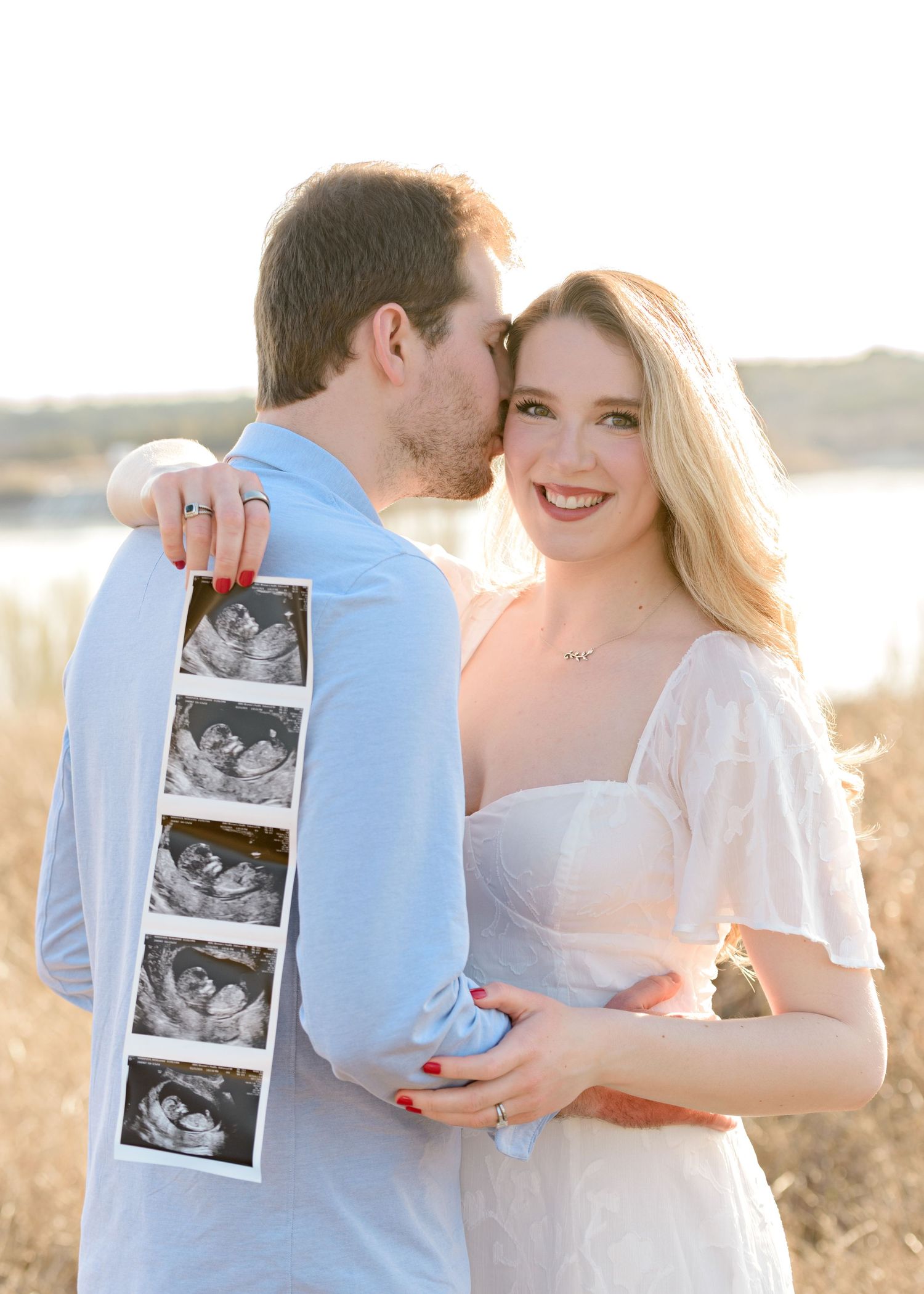 A couple holds ultrasound photos during sunset pregnancy announcement photoshoot in a golden field.