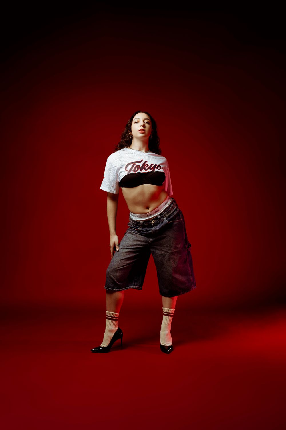 Dancer in crop top and baggy pants poses against dramatic red backdrop.