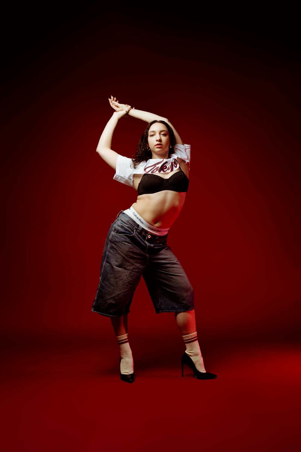 Dynamic dance pose with arms raised against red background.