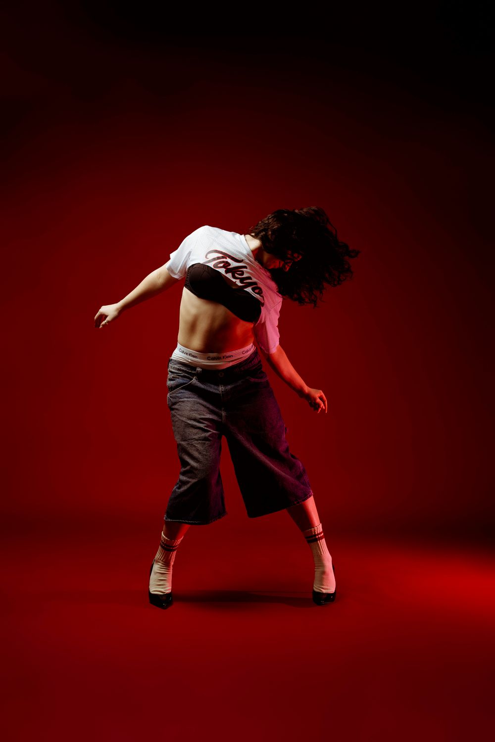 Dramatic dance pose with hair in motion against red backdrop.