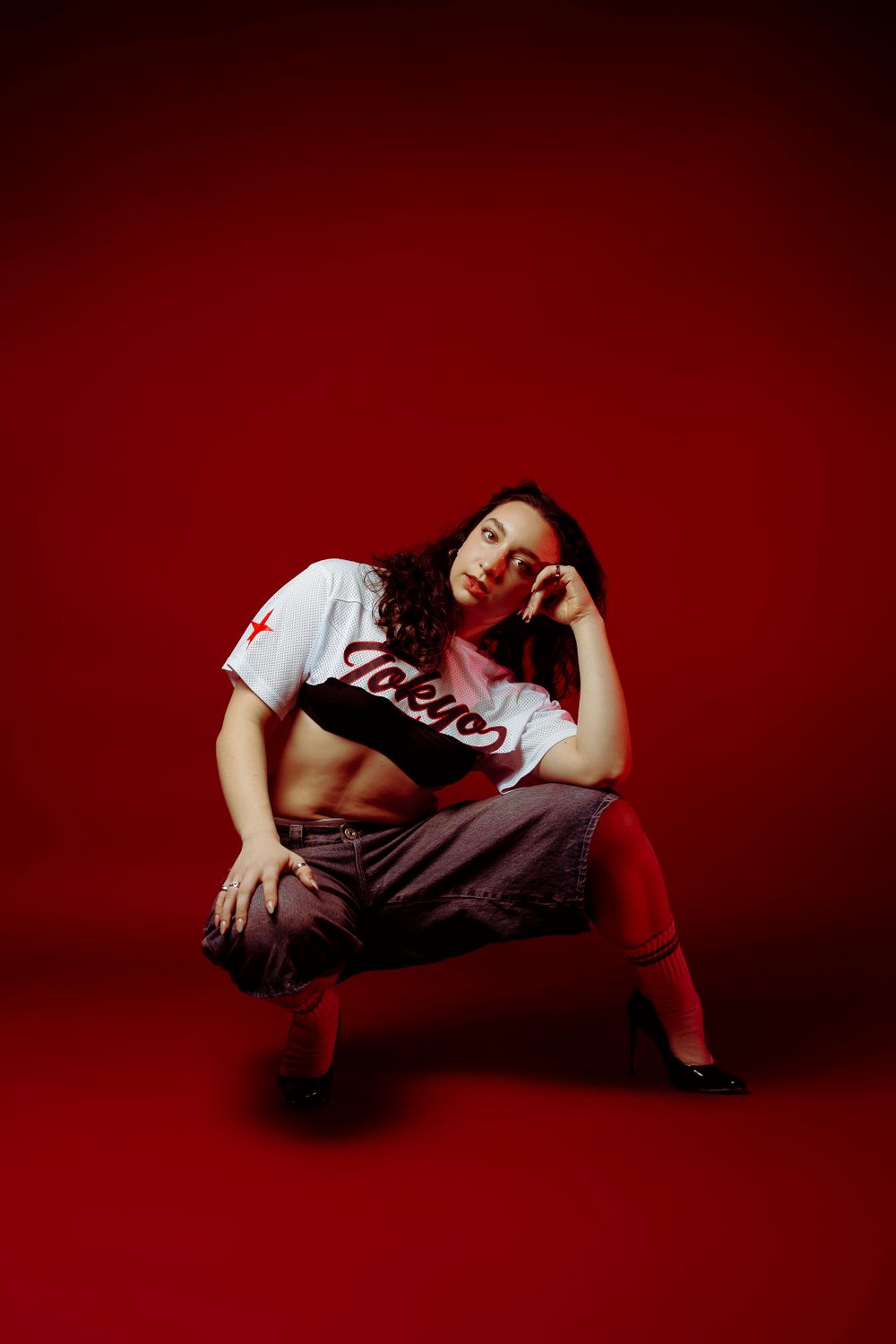 Athletic model crouches in casual streetwear and red socks against crimson background.