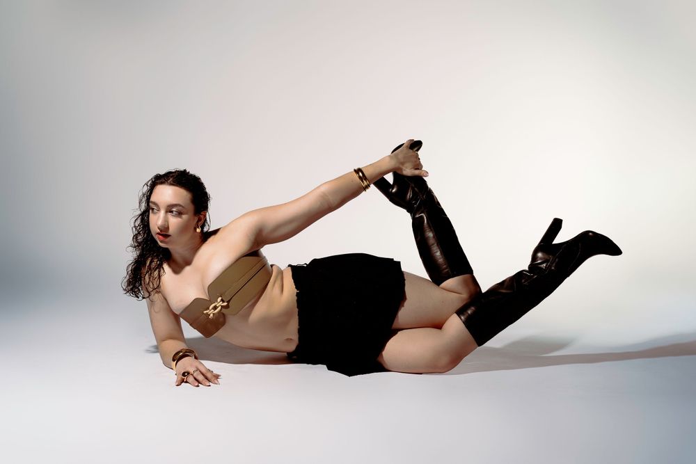 Model in beige top and black skirt poses dramatically on studio floor.