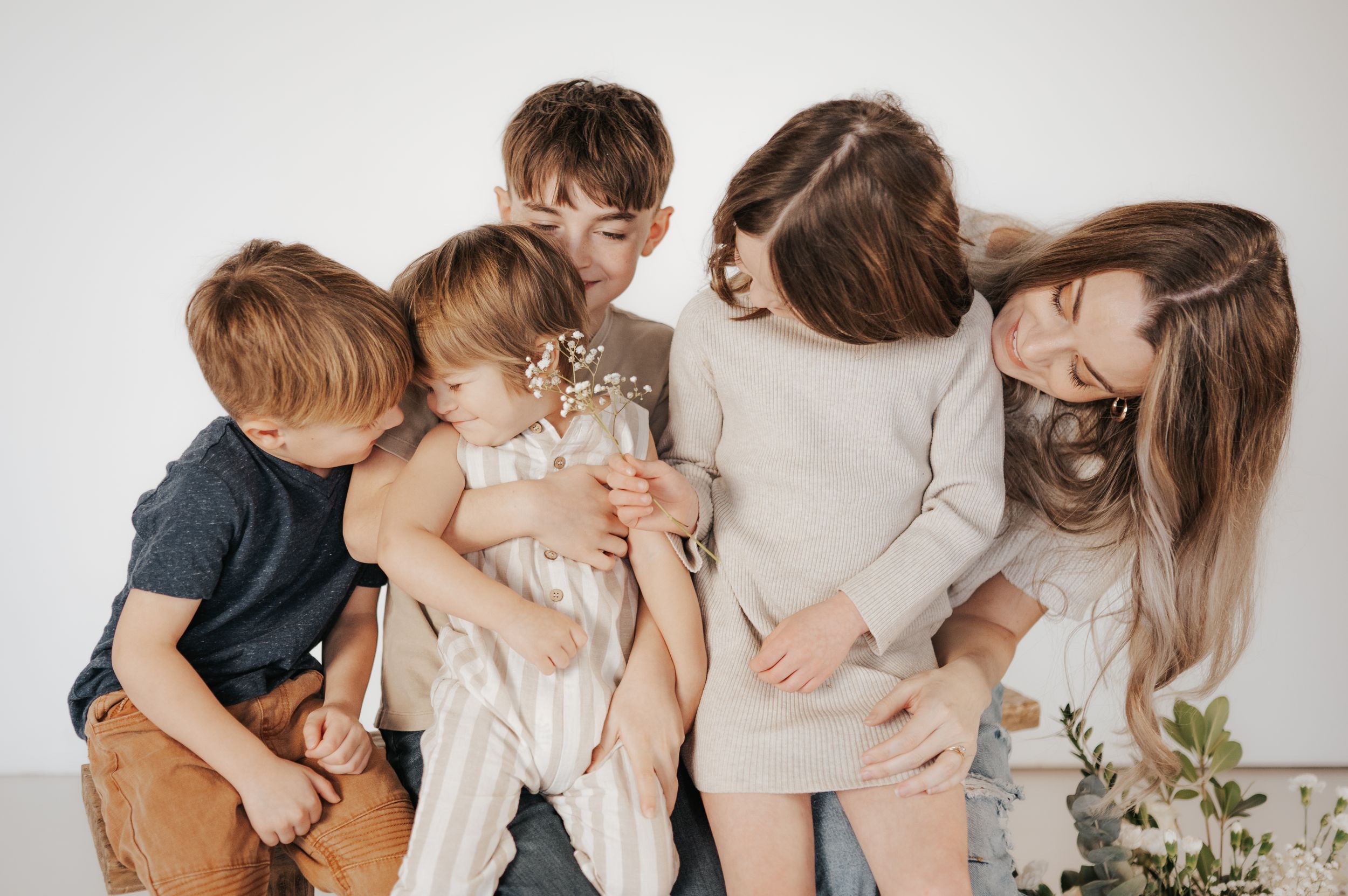 A heartwarming family portrait in soft neutral tones against a white backdrop with delicate greenery accents.