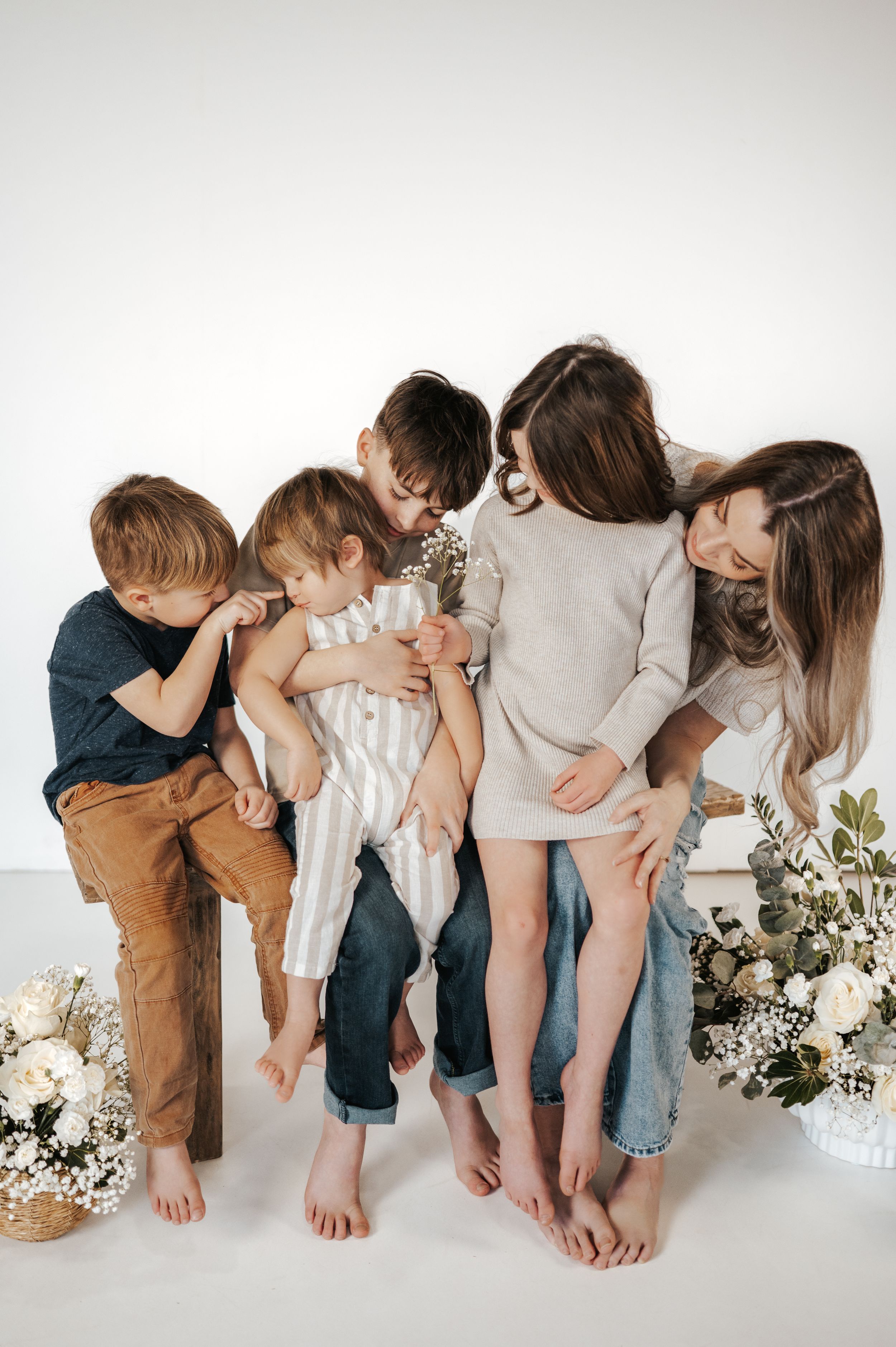 A group of children in casual clothing huddling and laughing together barefoot against a white background with floral decor.