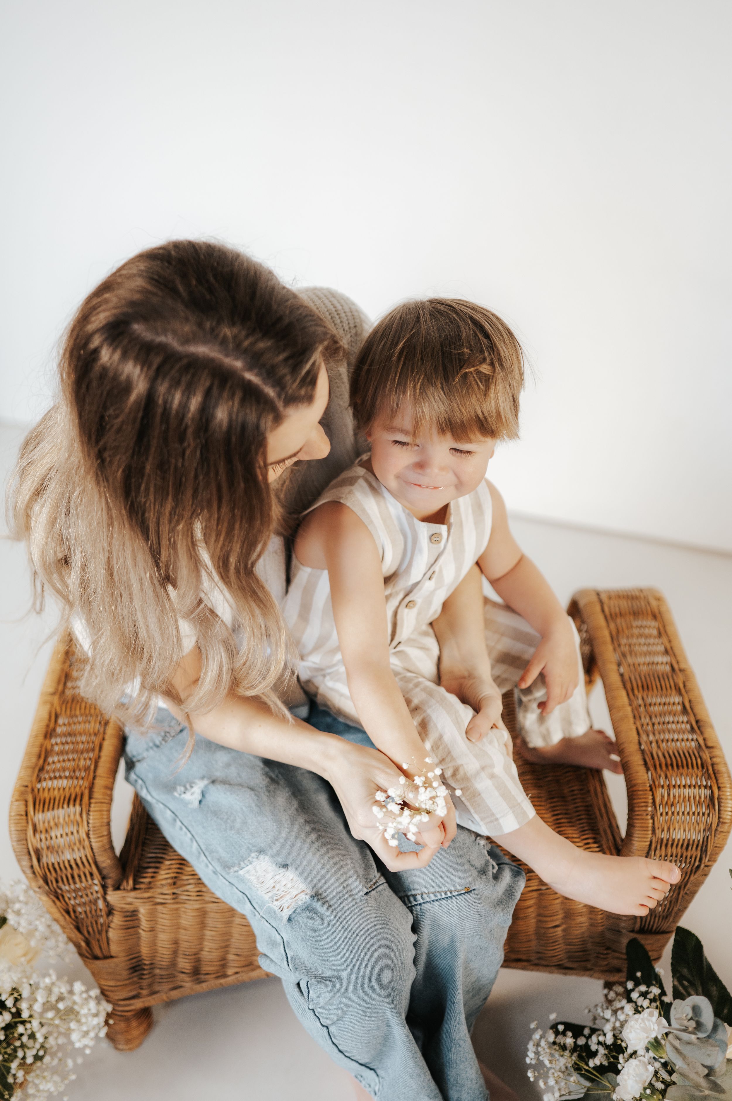 Sweet candid moment captured on wicker chair showing loving parent-child interaction with baby's breath flowers nearby.
