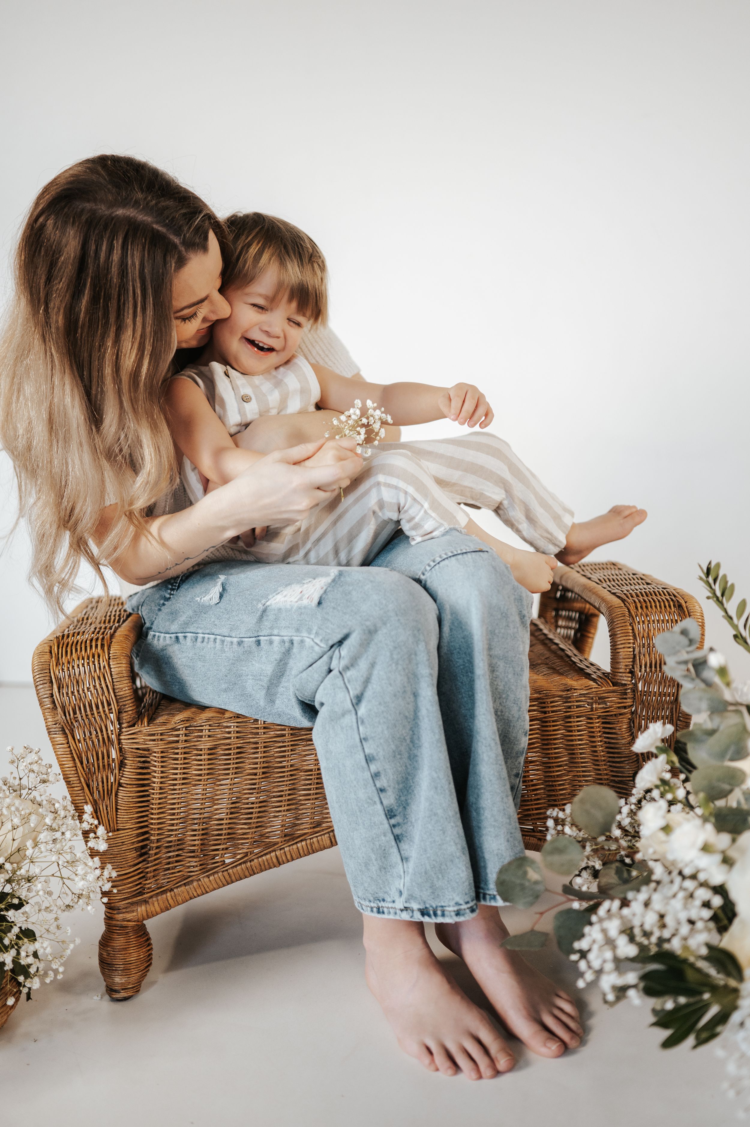 Sweet bonding moment on wicker chair with beautiful floral arrangements and light natural backdrop.