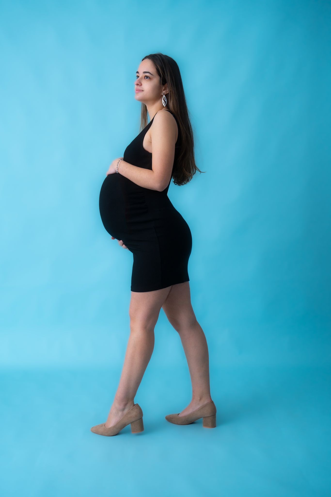 Maternity photoshoot against blue backdrop showing woman in black dress striking artistic poses.