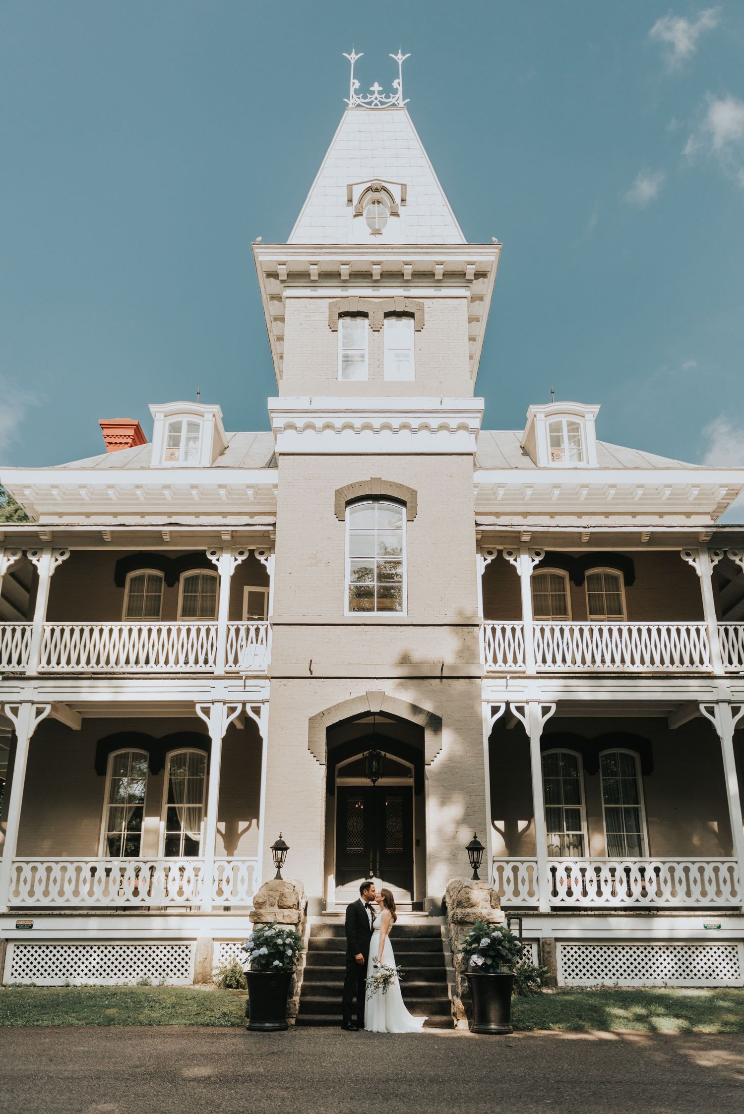 Elegant Victorian-style mansion with white exterior, featuring ornate tower and wrap-around porches with decorative railings.