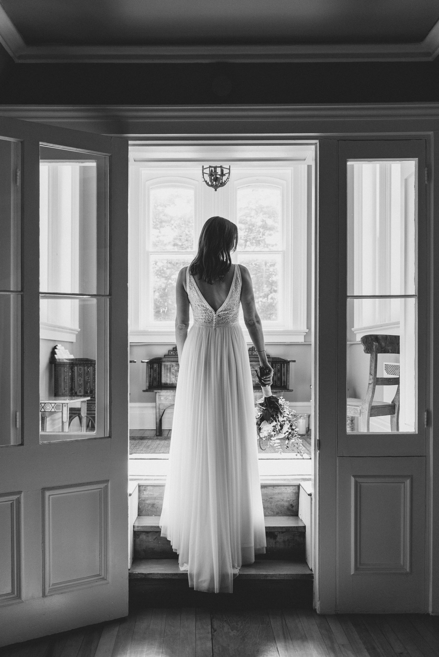 Black and white photo of figure in flowing white dress standing in vintage doorway with window panels.