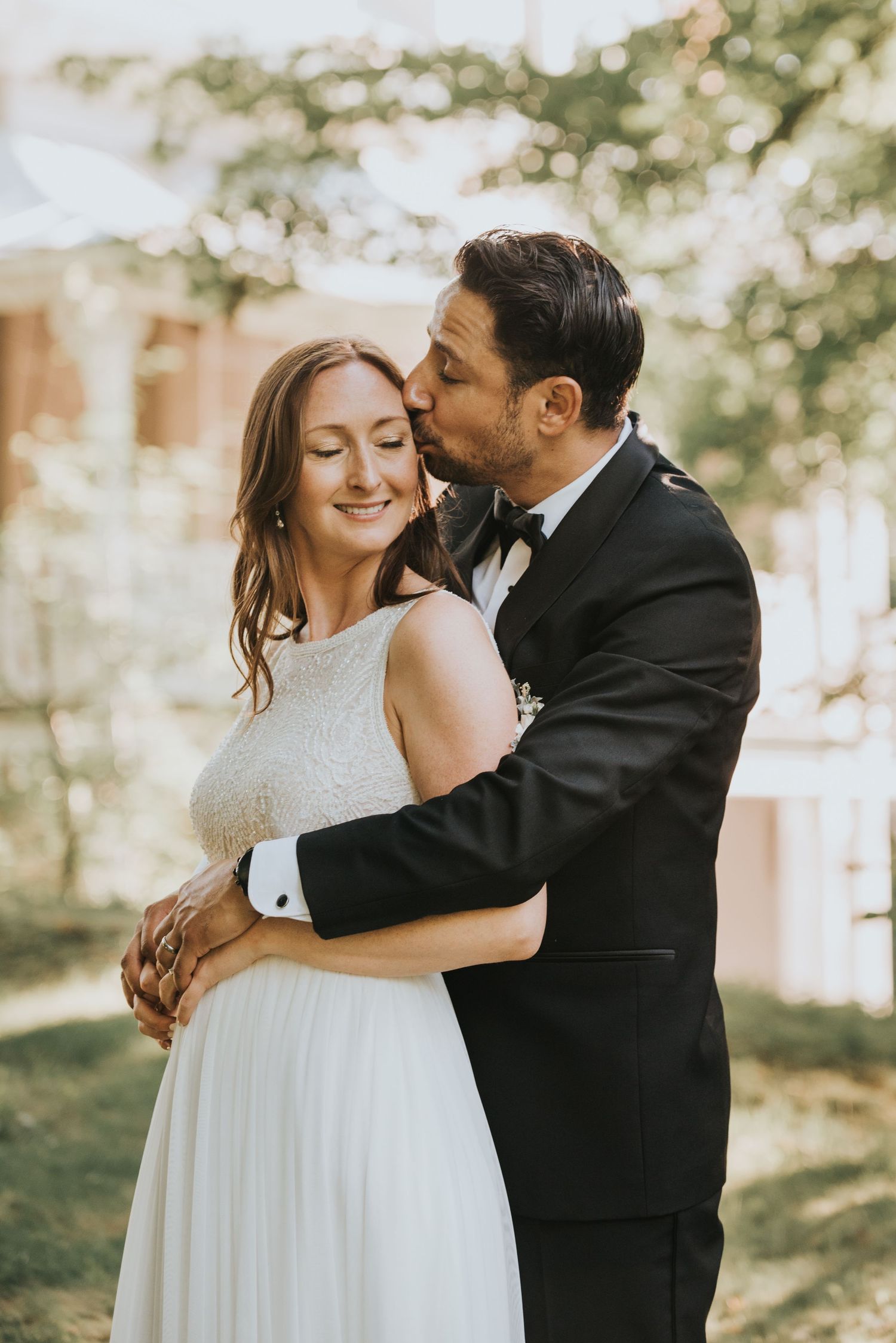 A romantic outdoor wedding moment with a couple embracing in formal attire under soft natural lighting.