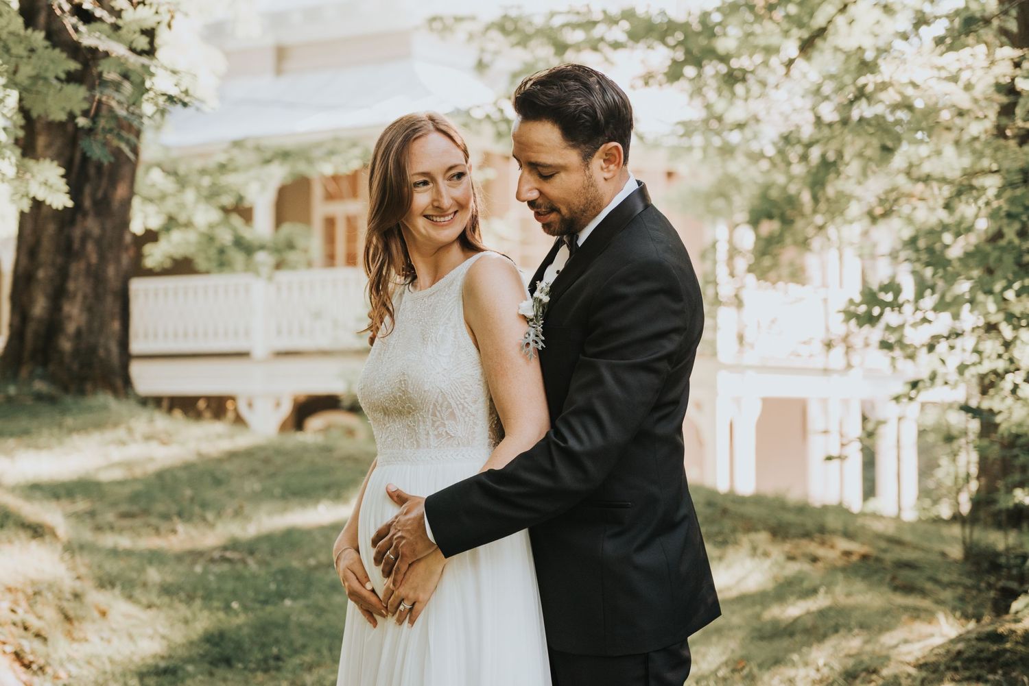 A couple shares a tender moment outdoors at their wedding celebration, with the bride in white and groom in black suit.