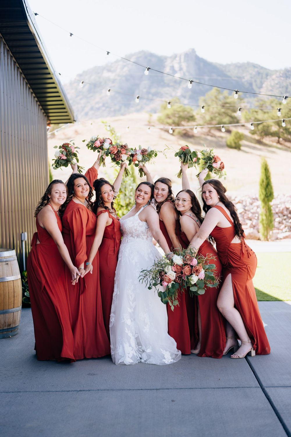 Wedding party in burgundy dresses and white gown pose together against desert mountain backdrop at outdoor venue.