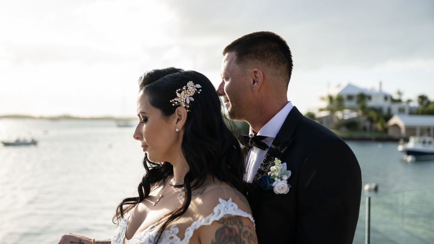 A romantic wedding couple enjoying a moment together on a waterfront terrace.