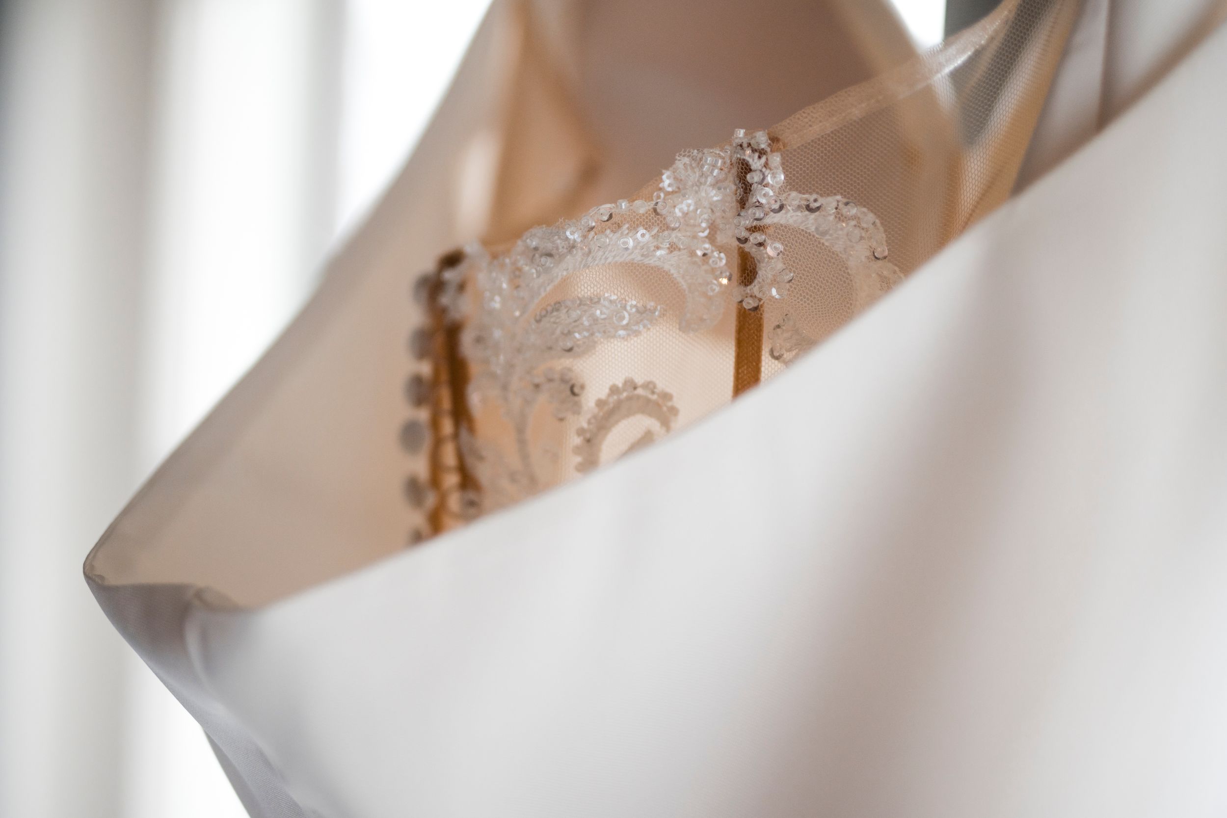 A delicate white lace wedding dress hangs elegantly against a soft background.