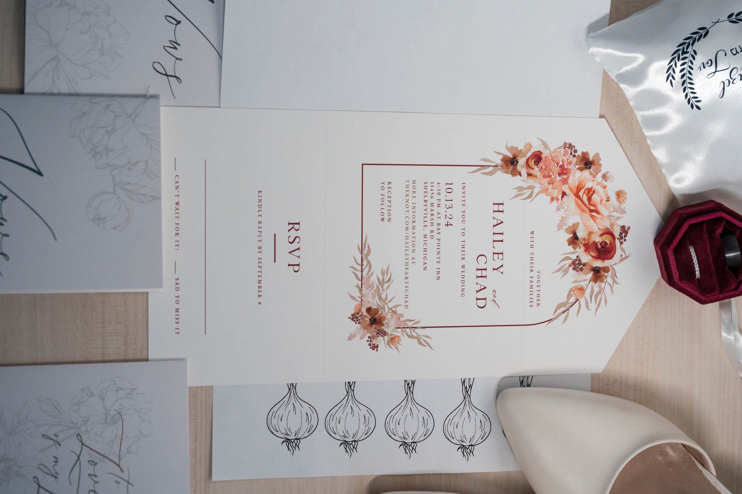 A wedding invitation with floral details and wax seal lies arranged with other paper elements.