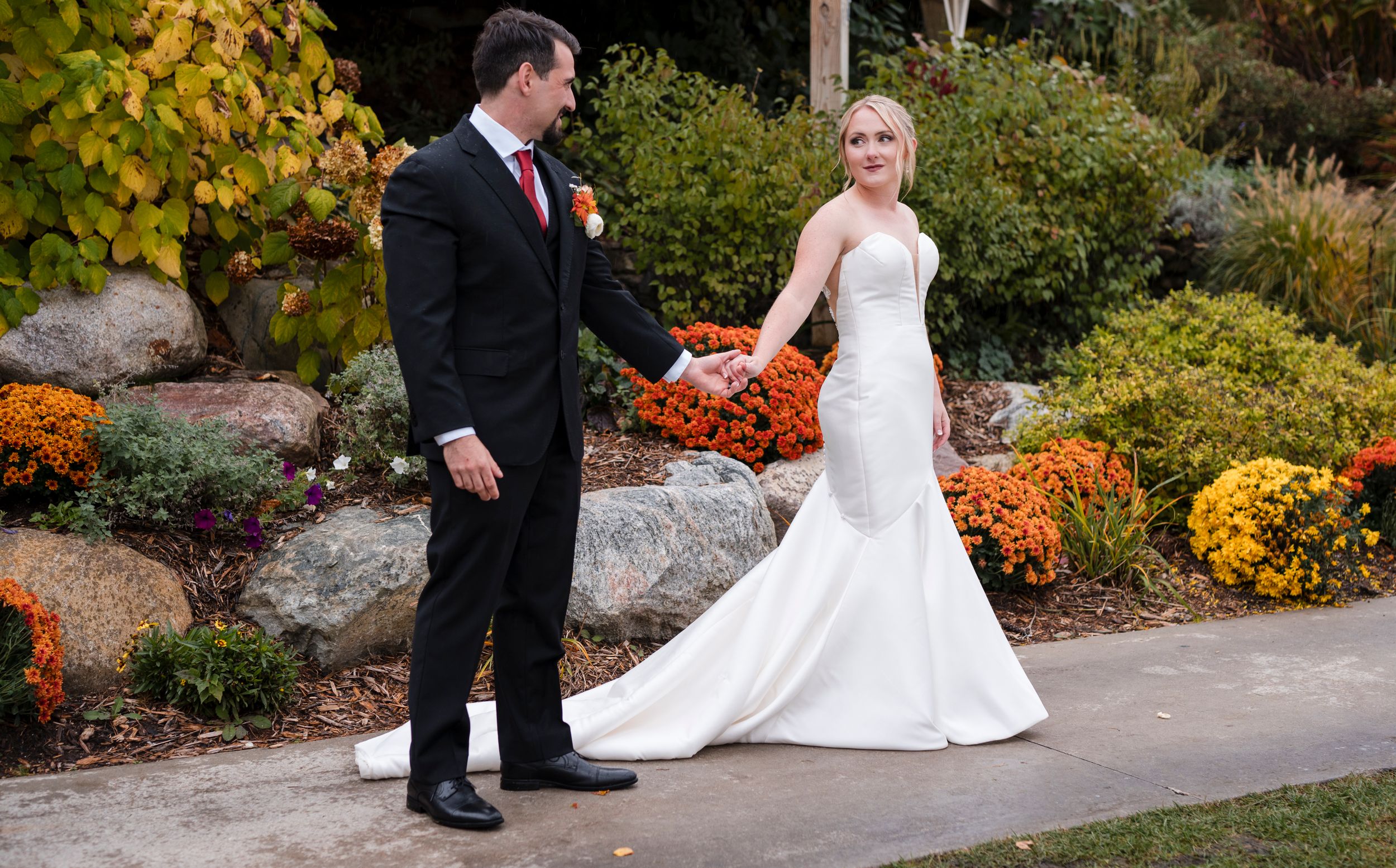 A bride and groom share a moment in a garden setting with vibrant autumn flowers.