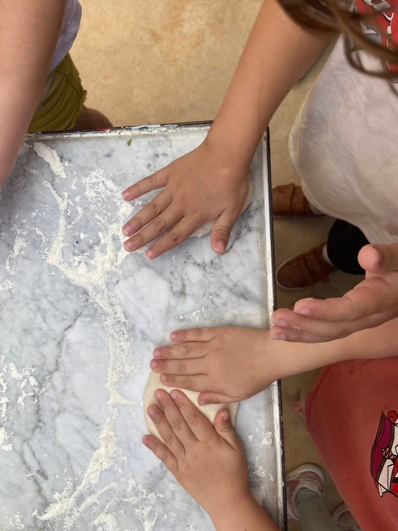 Small hands press into flour spread across a metal baking tray during a cooking activity.