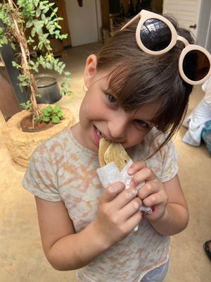 A young person enjoying a manakish snack outdoors with sunglasses perched on their head and potted plants nearby.