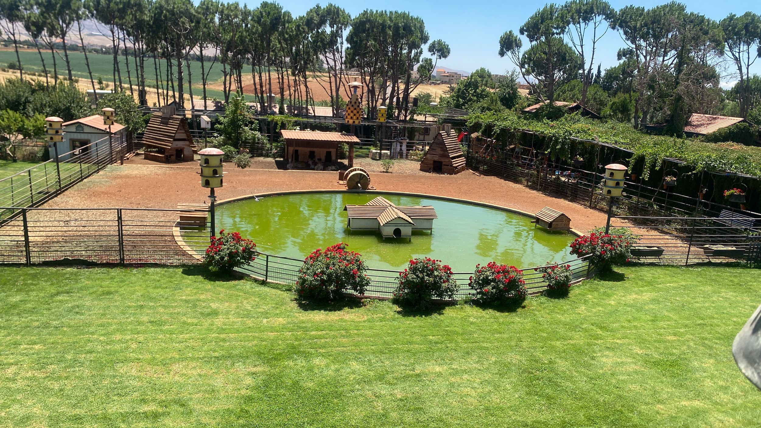 A landscaped courtyard features a green pond surrounded by manicured lawns, trees, and walking paths.