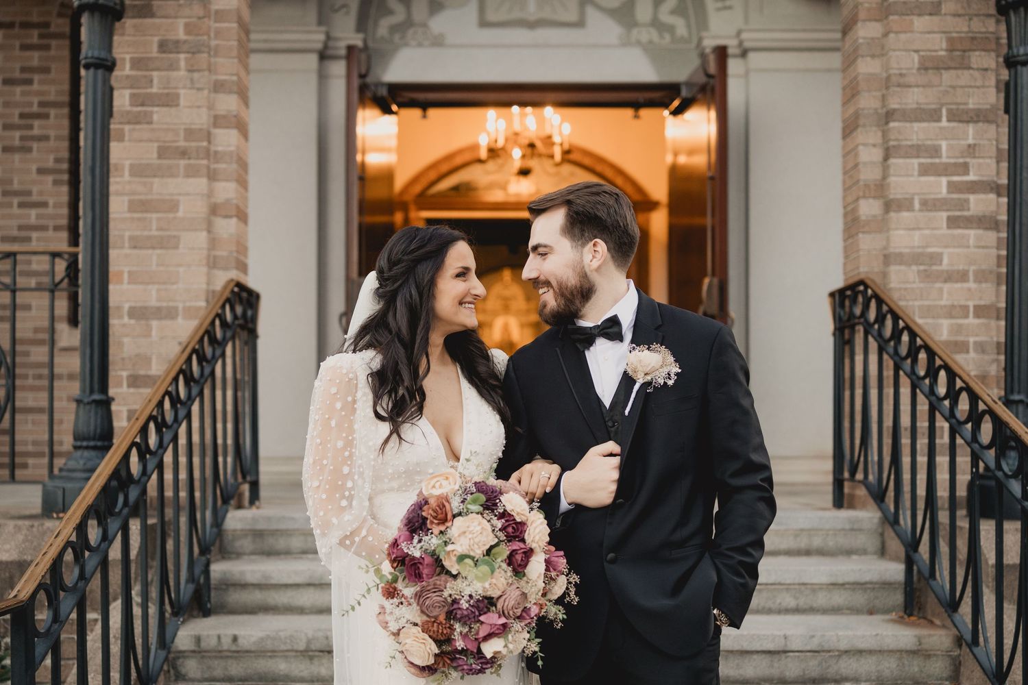 Newlyweds share a romantic moment outside a brick building with classical architectural details.