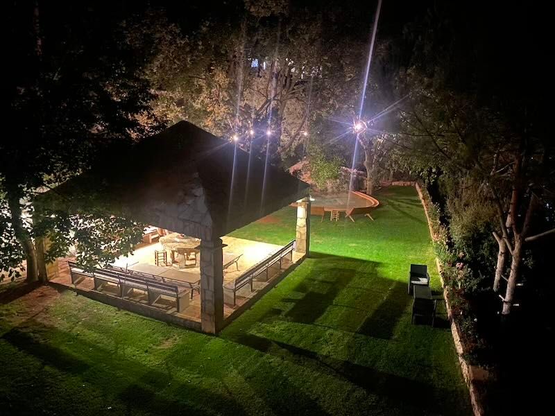 Illuminated outdoor pavilion at night with bright lights and manicured lawn surrounded by trees.