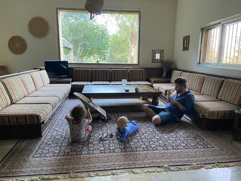 People enjoy a calm morning on a patterned rug in a sunlit living room with built-in seating.