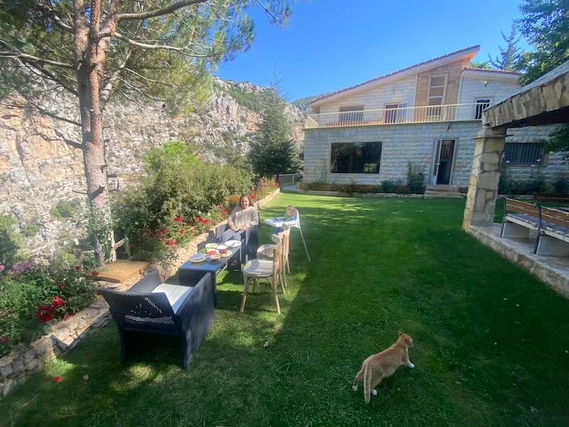 Modern backyard with outdoor seating, manicured lawn, and stone walls beneath blue sky.